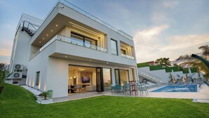 Ein modernes, zweistöckiges Haus mit Balkon, Swimmingpool und gepflegtem Rasen.