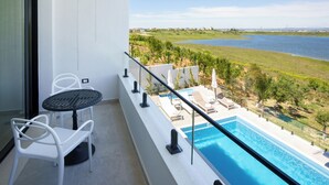 Ein Balkon mit Pool, weißen Stühlen und Blick auf einen See sowie entfernte Gebäude.