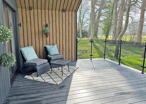 A wooden deck with two chairs and a table, a hanging plant, and a view of a grassy field. - The Woodland Boutique (Bassenthwaite, near Keswick)