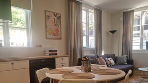 Una cucina moderna con mobili bianchi, un tavolo da pranzo con sottopiatti intrecciati e un divano con cuscini.