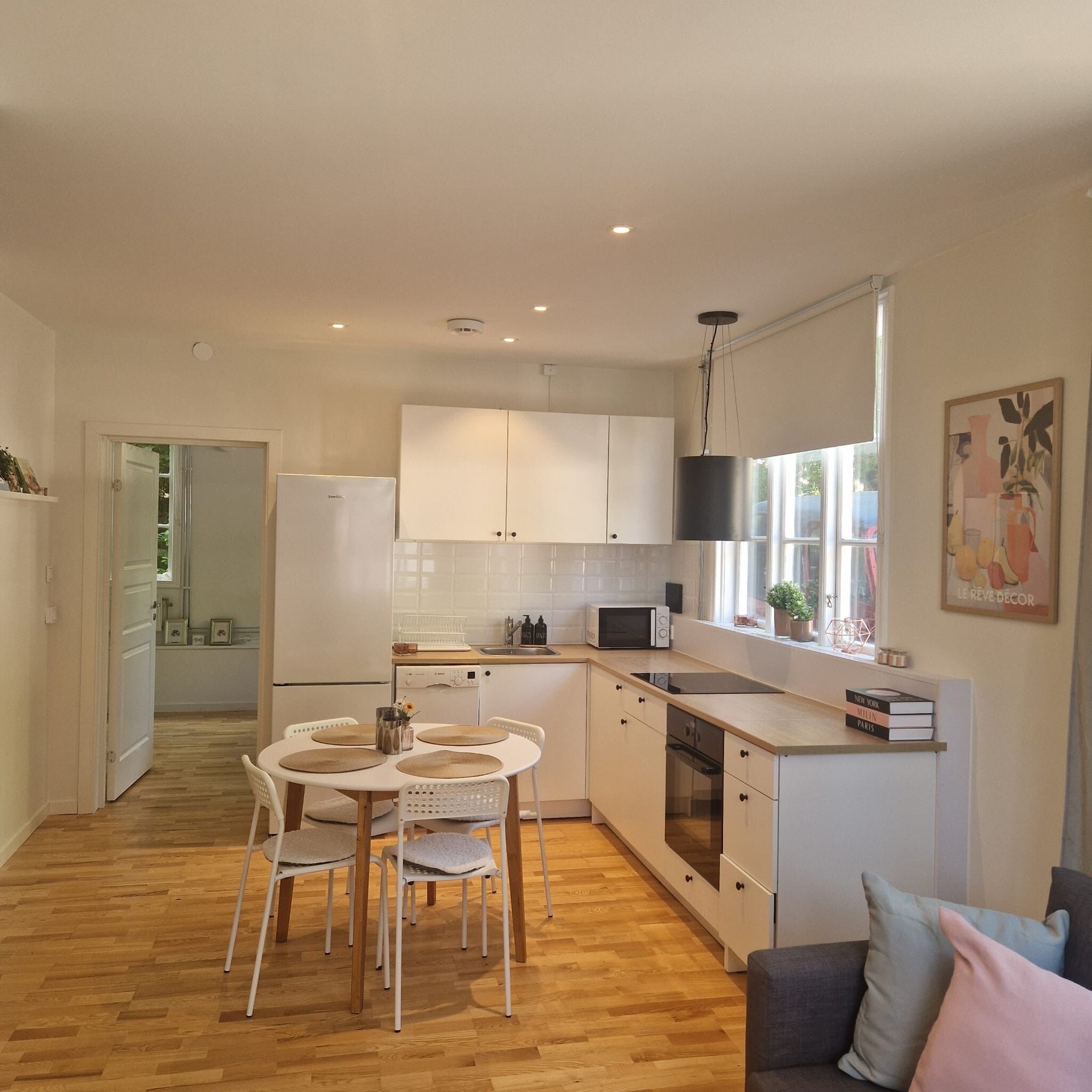 Une cuisine moderne avec des meubles blancs, une table à manger avec des chaises et un four encastré.
