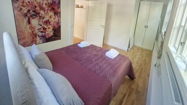 Una camera da letto con un letto, cuscini, un quadro, un armadio e un termosifone.