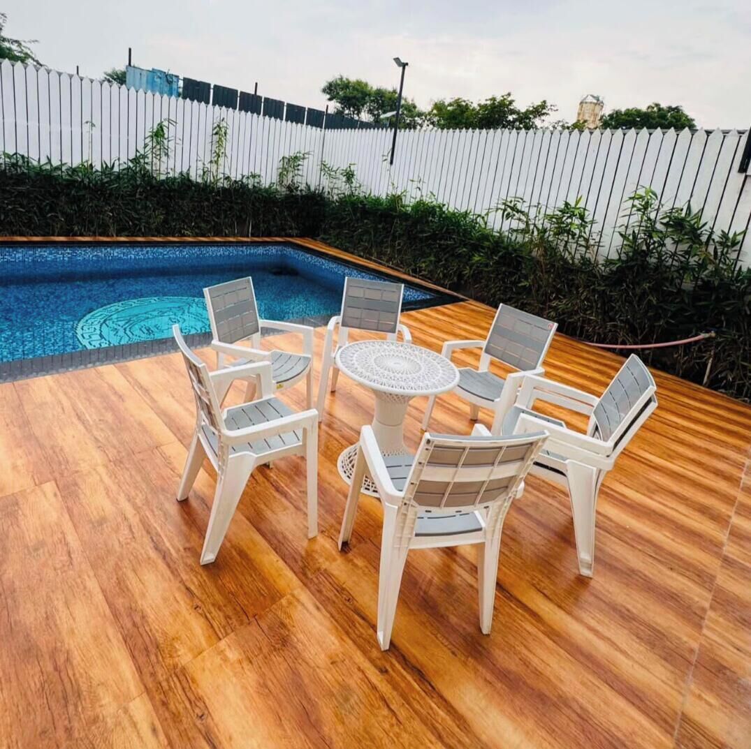Zona junto a la piscina con terraza de madera, una mesa redonda con sillas y una valla blanca al fondo.