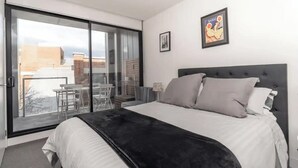 Ein Schlafzimmer mit einem großen Bett, einer Glasschiebetür zu einem Balkon und einem gerahmten Bild an der Wand.