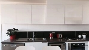 Eine moderne Küche mit weißen Schränken, einer schwarzen Spritzschutzwand, Edelstahlgeräten und einem Topfpflanze.