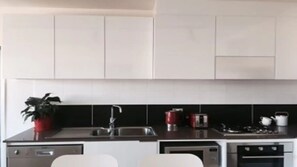 A modern kitchen with white cabinets, a black backsplash, stainless steel appliances, and a potted plant. - Stylish 2BDR Retreat in Vibrant Abbotsford (Abbotsford)