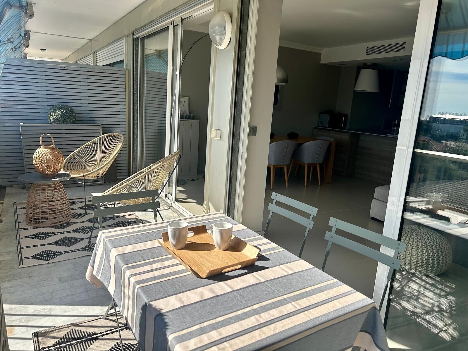 An outdoor patio with a striped table, wicker chairs, and a dining area with chairs and a table.