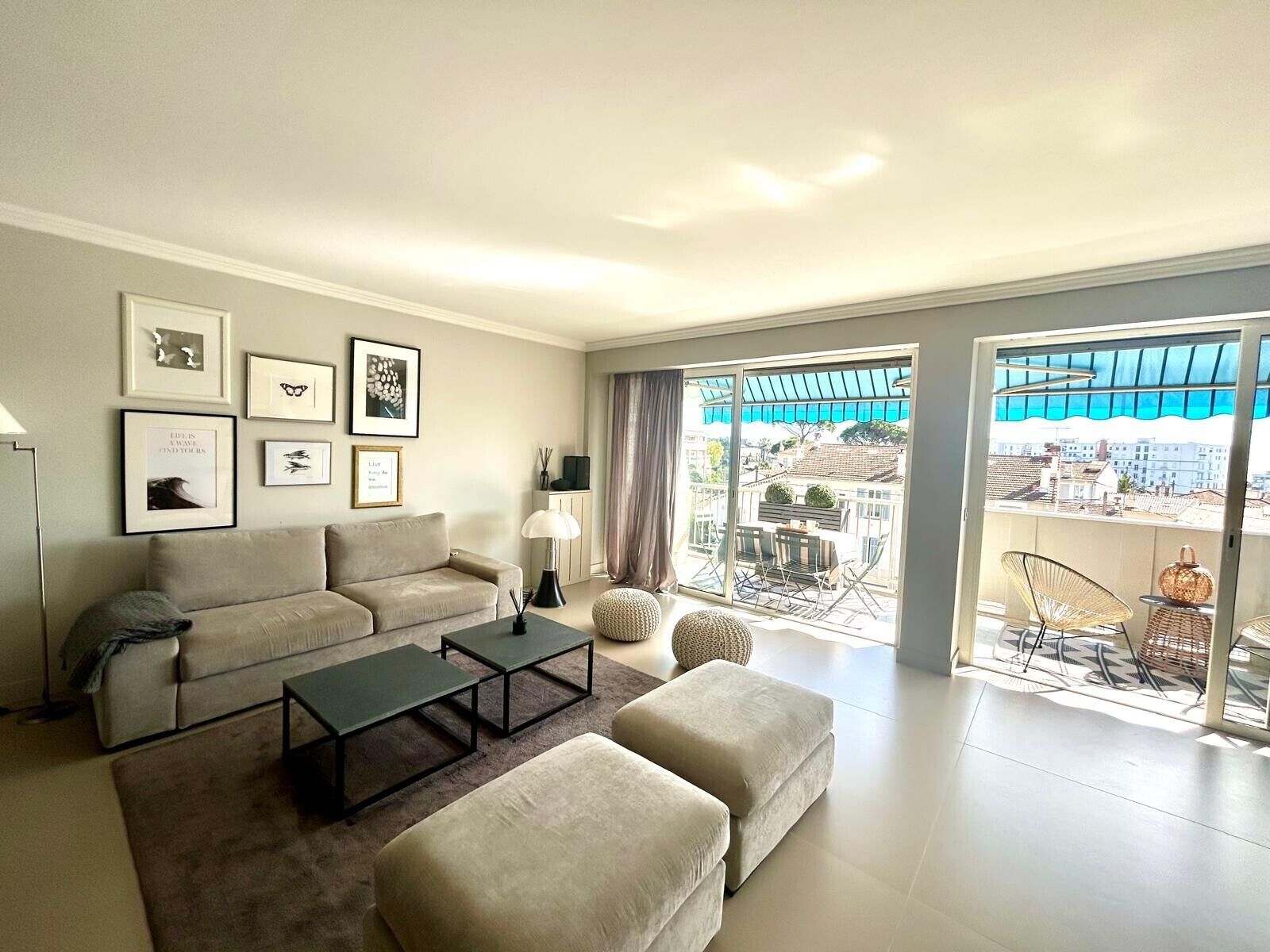 Un salon moderne comprenant un canapé, un pouf, une table basse et donnant sur un balcon aménagé avec du mobilier d’extérieur.