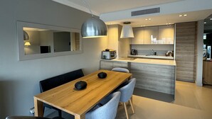 Eine moderne Küche mit Essbereich, ausgestattet mit einem Holztisch, grau gepolsterten Stühlen und Pendelleuchten.
