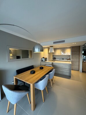A modern kitchen with a dining area, featuring a wooden table, grey upholstered chairs, and pendant lighting. - Apartment 'D&L Sea View' with Private Terrace, Wi-Fi and Air Conditioning (Cannes)