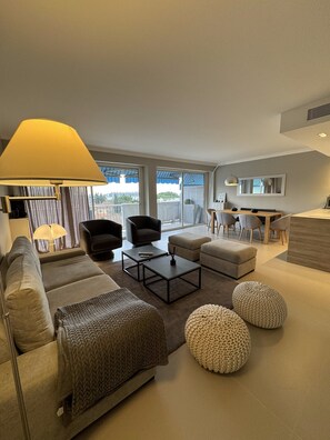 A modern living room with a sofa, armchairs, ottomans, a coffee table, and a dining area with chairs and a table. - Apartment 'D&L Sea View' with Private Terrace, Wi-Fi and Air Conditioning (Cannes)