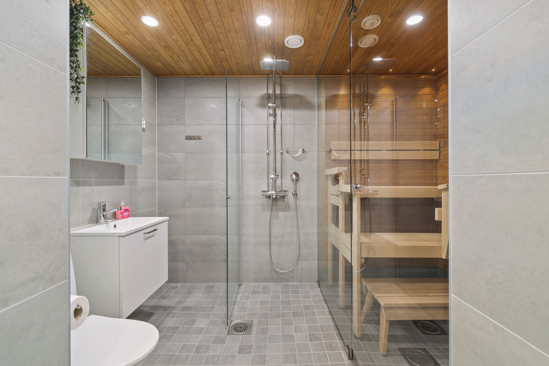 Un baño moderno con ducha envuelta en vidrio, un lavamanos blanco y un banco de madera.