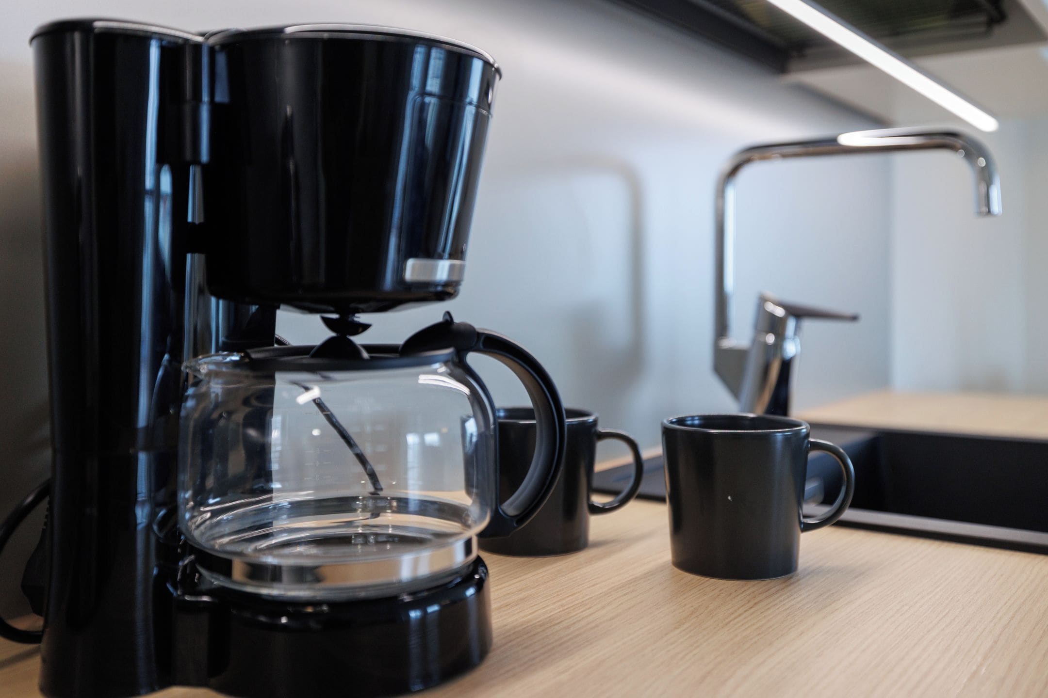 En kaffebryggare med en genomskinlig kanna och en svart mugg placerad på en träyta.