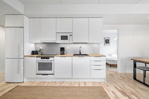 Una cocina moderna con armarios blancos, horno empotrado, cafetera y lavabo.