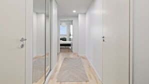 A hallway with a bed in the distance, a door on the left, and a rug on the floor. - New 2BR Apt with Sauna & Stunning Views  (Oulu)