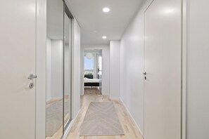 Un pasillo con una cama a lo lejos, una puerta a la izquierda y una alfombra en el suelo.