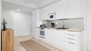 A modern kitchen with white cabinets, a stainless steel oven, a microwave, and a sink. - New 2BR Apt with Sauna & Stunning Views  (Oulu)