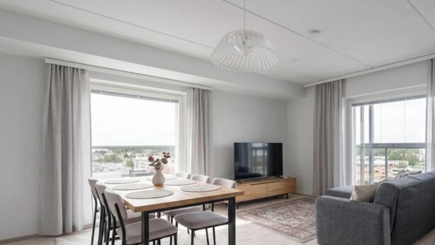 A modern living room with a dining area, large windows, a flat-screen TV, and a grey sofa. - New 2BR Apt with Sauna & Stunning Views  (Oulu)