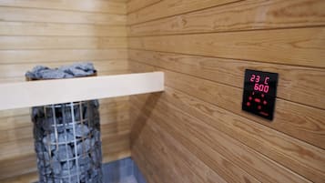 A sauna with a wooden interior, a digital display showing temperature and time, and a bench with a towel.