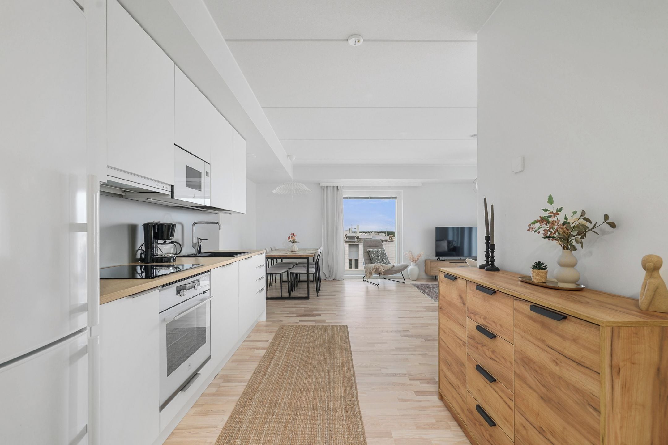 Une cuisine moderne avec des meubles blancs, une table à manger en bois et une vue sur le salon.
