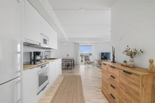 Una cocina moderna con armarios blancos, una mesa de comedor de madera y vistas al área de estar.
