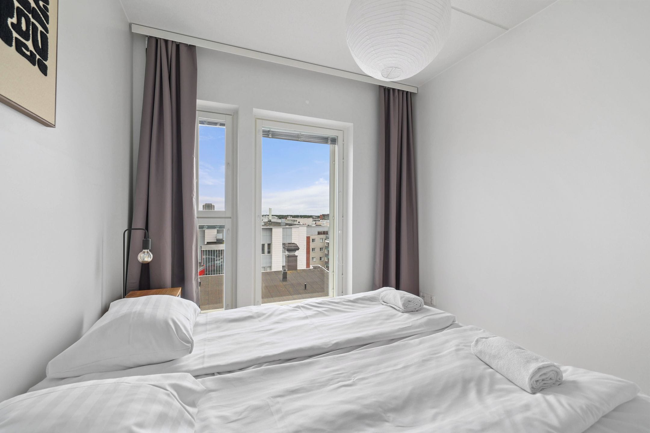 A hotel room with a bed, curtains, a window, and a view of the cityscape.