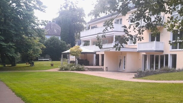Ein zweigeschossiges Gebäude mit einer überdachten Terrasse und einem gepflegten Rasen.