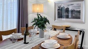 A dining area with a table set for four, a bottle of wine, and a potted plant. - Villa Boronia - 2 Bedroom Villa at Cypress Lakes Resort (POKOLBIN)