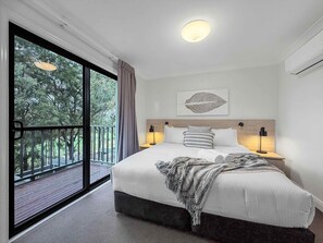 Ein Schlafzimmer mit einem großen Bett, Blick auf Bäume durch eine Schiebetür und einer Deckenleuchte.