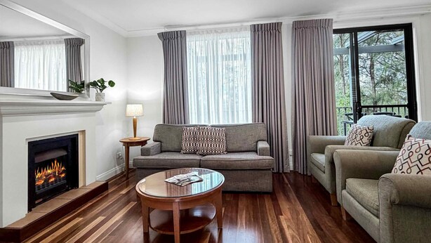 A living room with a fireplace, two sofas, a coffee table, and a large window with curtains. - Villa Boronia - 2 Bedroom Villa at Cypress Lakes Resort (POKOLBIN)