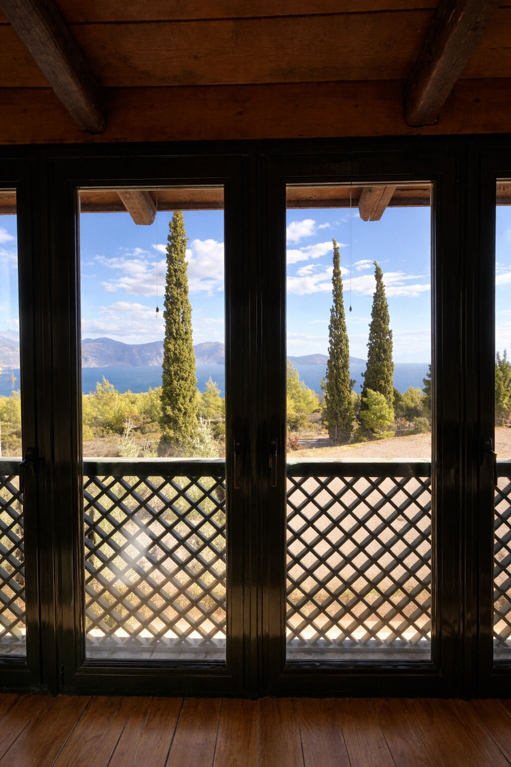 A wooden-framed window with a lattice design, offering a view of trees and mountains.