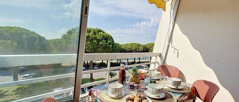 Un balcon avec une table dressée pour le dîner, donnant sur une étendue d’eau et sur la verdure.