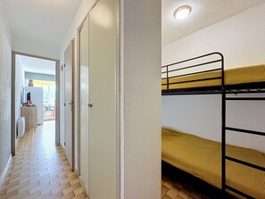 Ein Gang, der zu einem Raum mit Etagenbetten, einem Heizkörper und einer Tür führt.