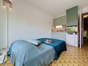 A compact bedroom with a bed, a small kitchenette, and a bathroom visible through an open door. - La Lagune by Interhome (Port Camargue)