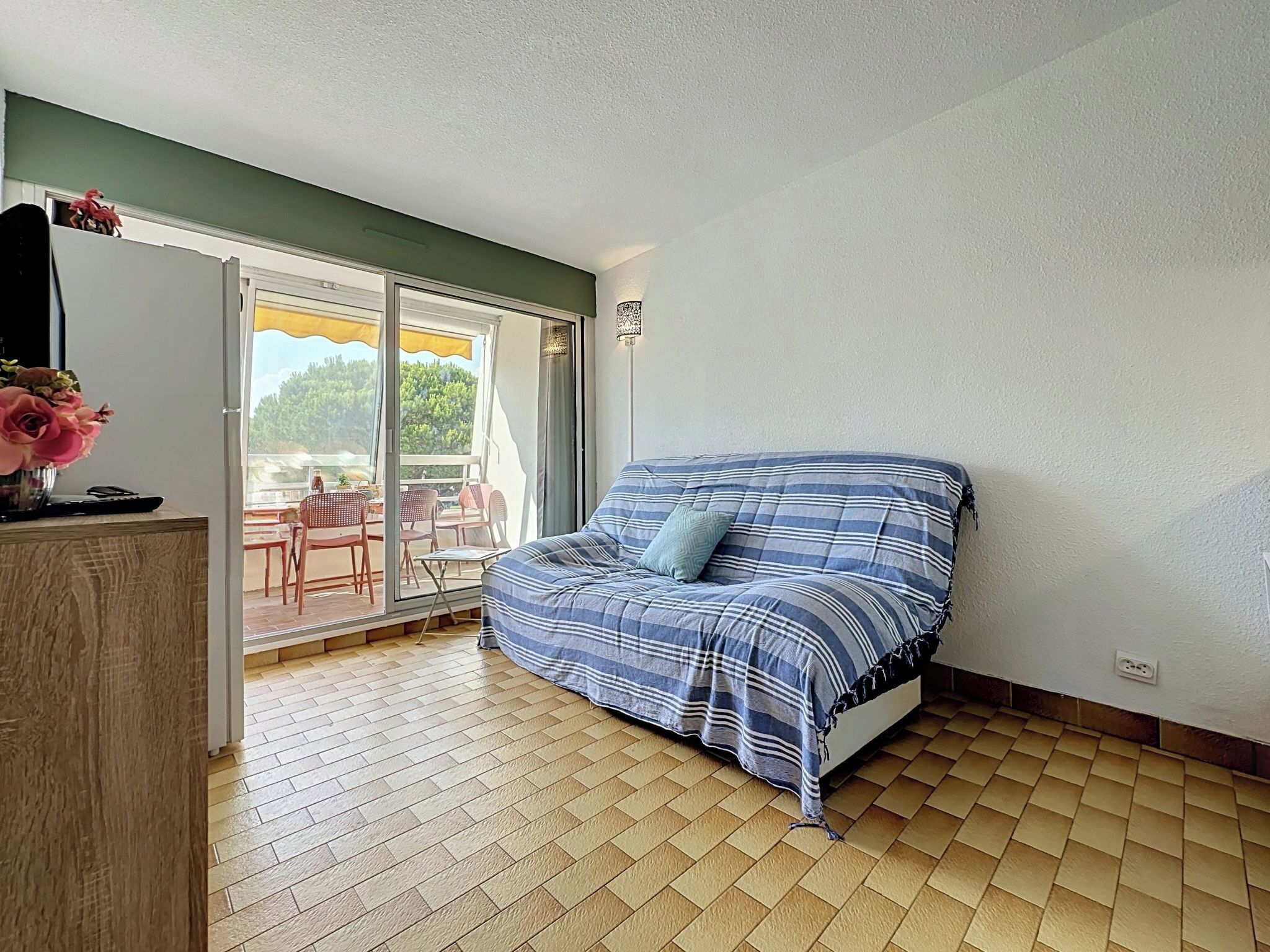 A bedroom with a bed, a wooden dresser, and a sliding glass door leading to an outdoor area with chairs and a table.