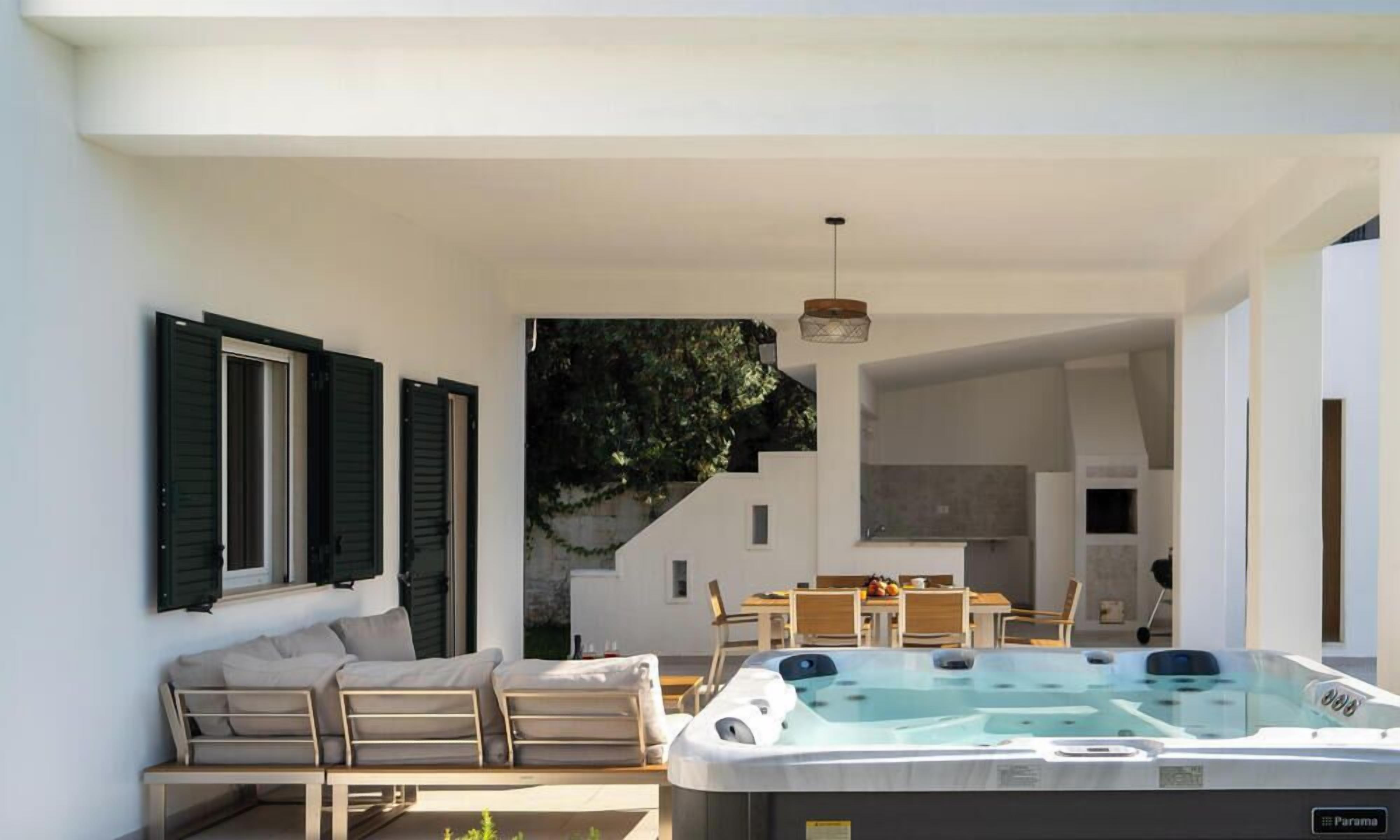 A modern outdoor living area with a hot tub, a sofa, and a dining table.