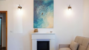 Ein Wohnzimmer mit Kamin, einem weißen Kaminumbau, einem beigen Sofa und einem großen abstrakten Gemälde darüber.