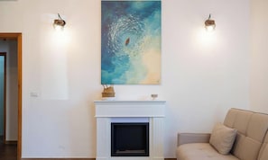 Ein Wohnzimmer mit Kamin, einem weißen Kaminumbau, einem beigen Sofa und einem großen abstrakten Gemälde darüber.