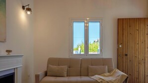 Ein Zimmer mit einem beigefarbenen Sofa, einer Holztür und einem Fenster mit Blick auf Grünflächen.