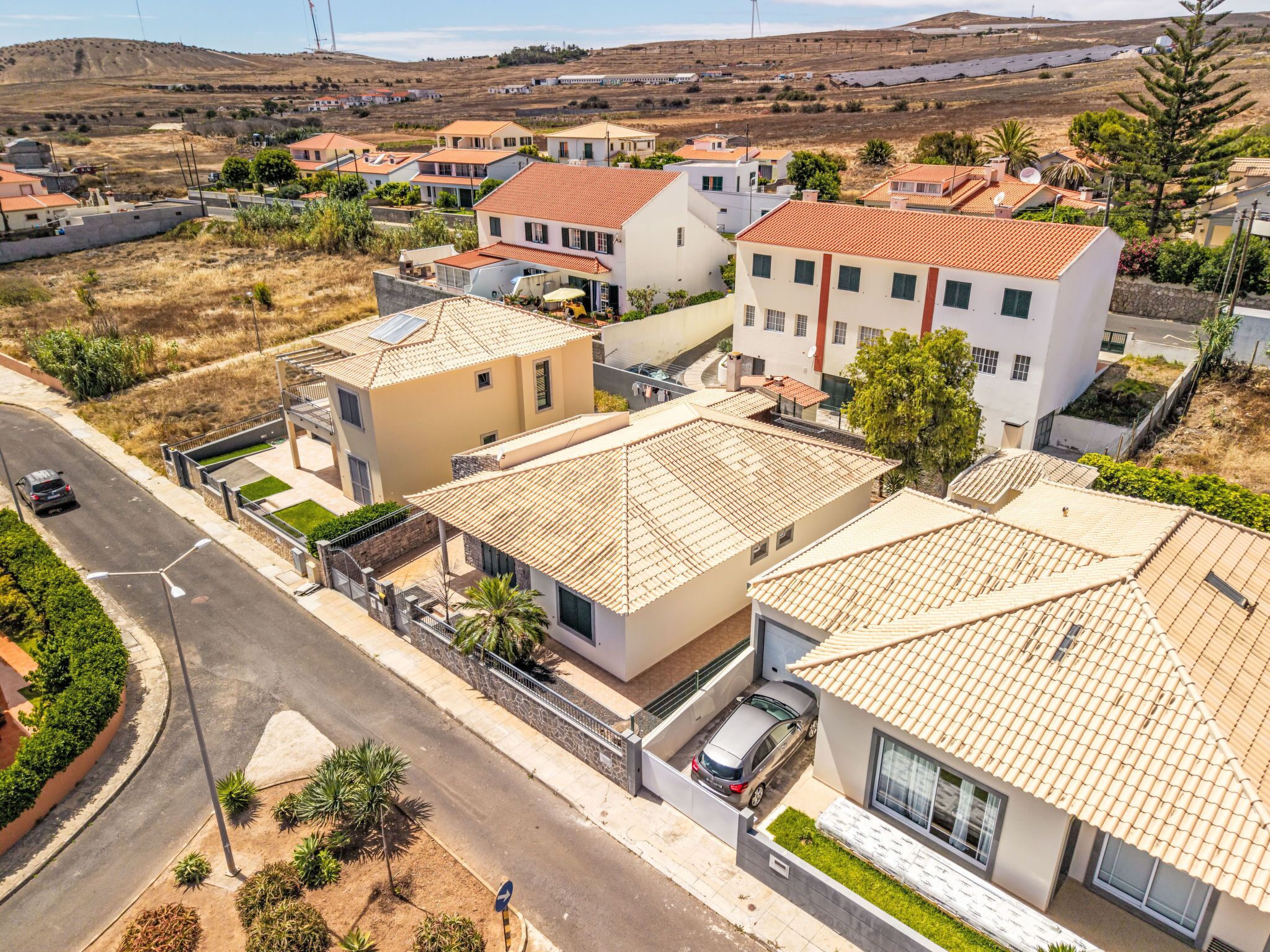 A residential area with houses featuring red-tiled roofs, a street, and a hilly landscape in the background.