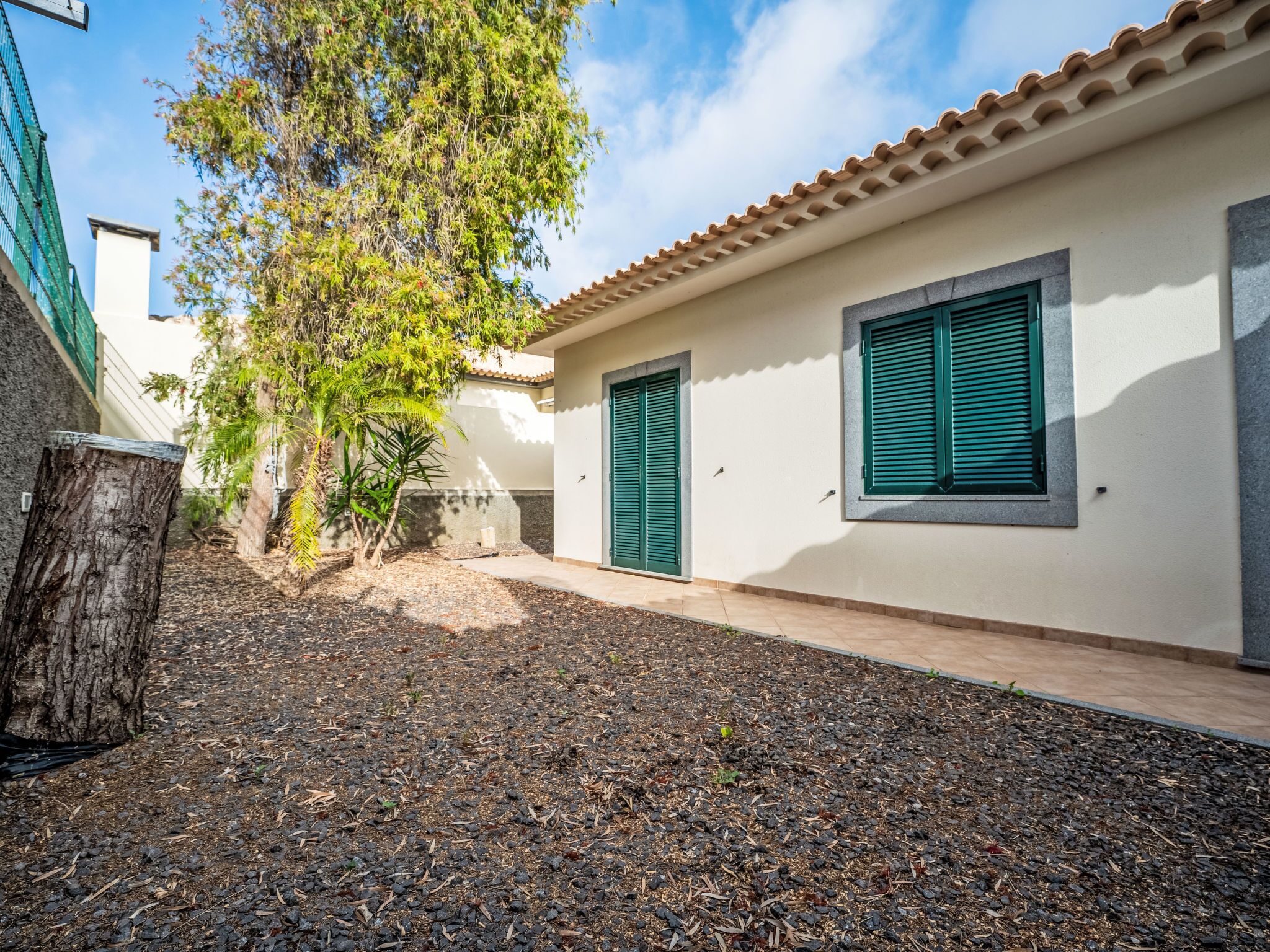 A building with a tiled roof, a tree, and a gravel pathway.