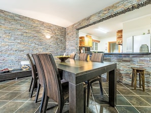 A dining area with a stone wall, a dark wooden table, and matching chairs. - Villa Rosa by Interhome (Porto Santo)