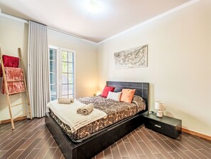 A modern bedroom with a large bed, a nightstand, a lamp, and a window with curtains. - Villa Rosa by Interhome (Porto Santo)