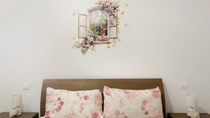 Een slaapkamer met een bed, twee nachtkastjes, een raam met bloemendecoratie en een lichtschakelaar.