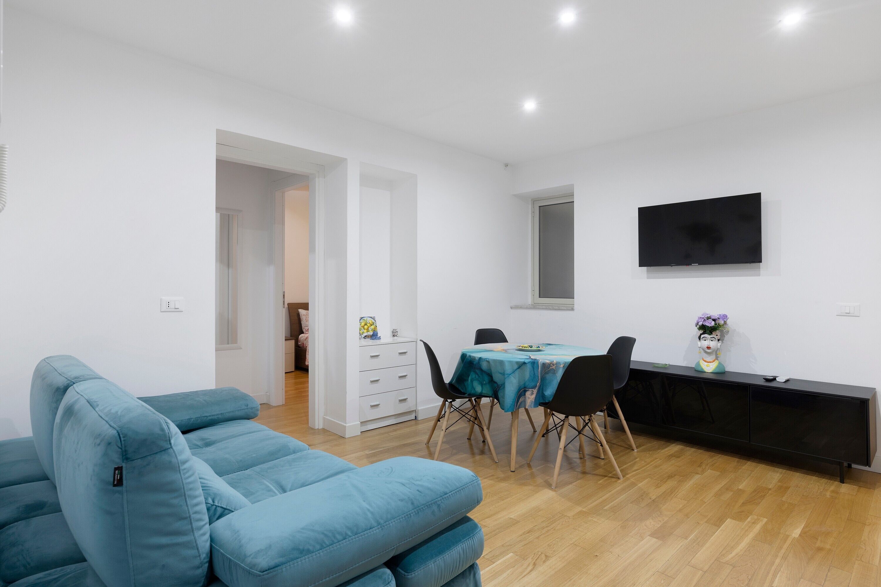 Ein modernes Wohnzimmer mit einem blauen Sofa, einem Esstisch mit Stühlen und einem an der Wand montierten Flachbildfernseher.