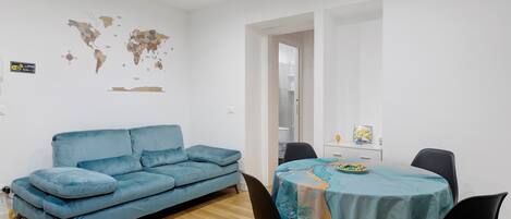 Ein modernes Wohnzimmer mit einem blauen Sofa, einem Esstisch mit Stühlen und einer Weltkarte an der Wand.
