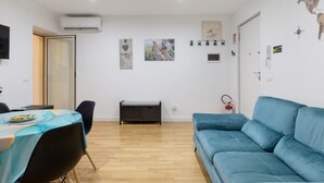 Een woonkamer met een blauwe bank, een eettafel met stoelen en een kleine bankje.