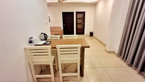 A dining area with a wooden table and white chairs, a coffee maker, and a water dispenser on the table. - Hotel Wayanad gate (Vythiri)