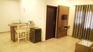 A compact living space with a kitchenette, a door, a television mounted on a wooden panel, and a curtain. - Hotel Wayanad gate (Vythiri)