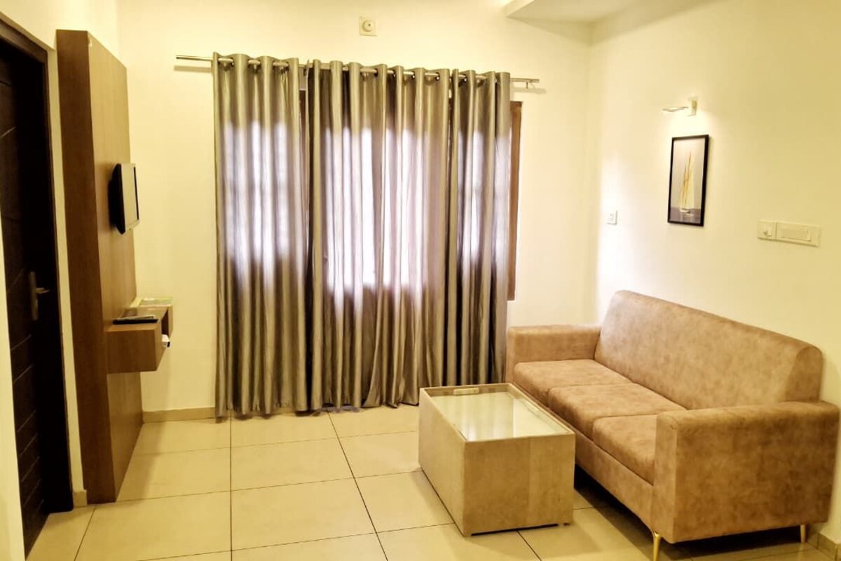 Una sala de estar con un sofá color beige, una mesa de centro de vidrio y una cortina.